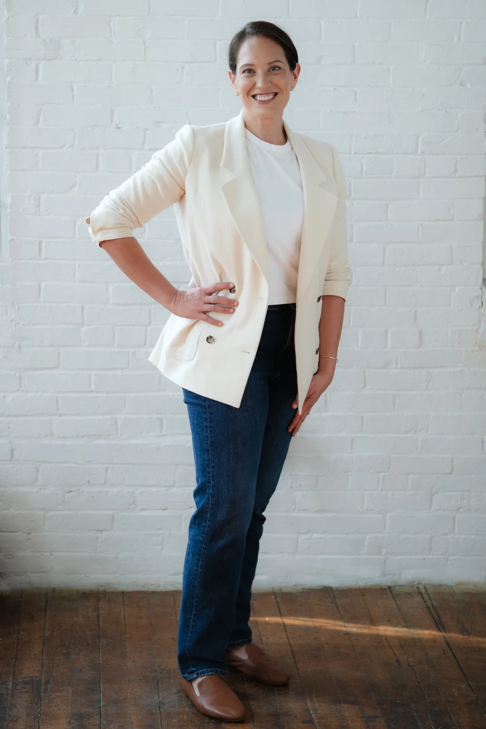 Annie Wright standing by a white brick wall, wearing a cream blazer.