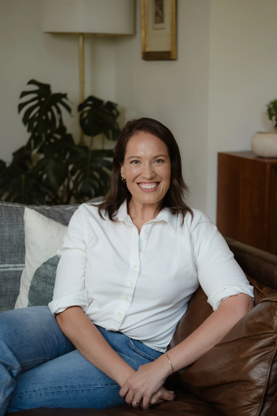 Annie Wright smiling at the camera, seated on a sofa in a white blouse.