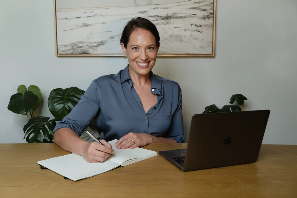 Annie Wright writing in a notebook at her desk with a laptop beside her.