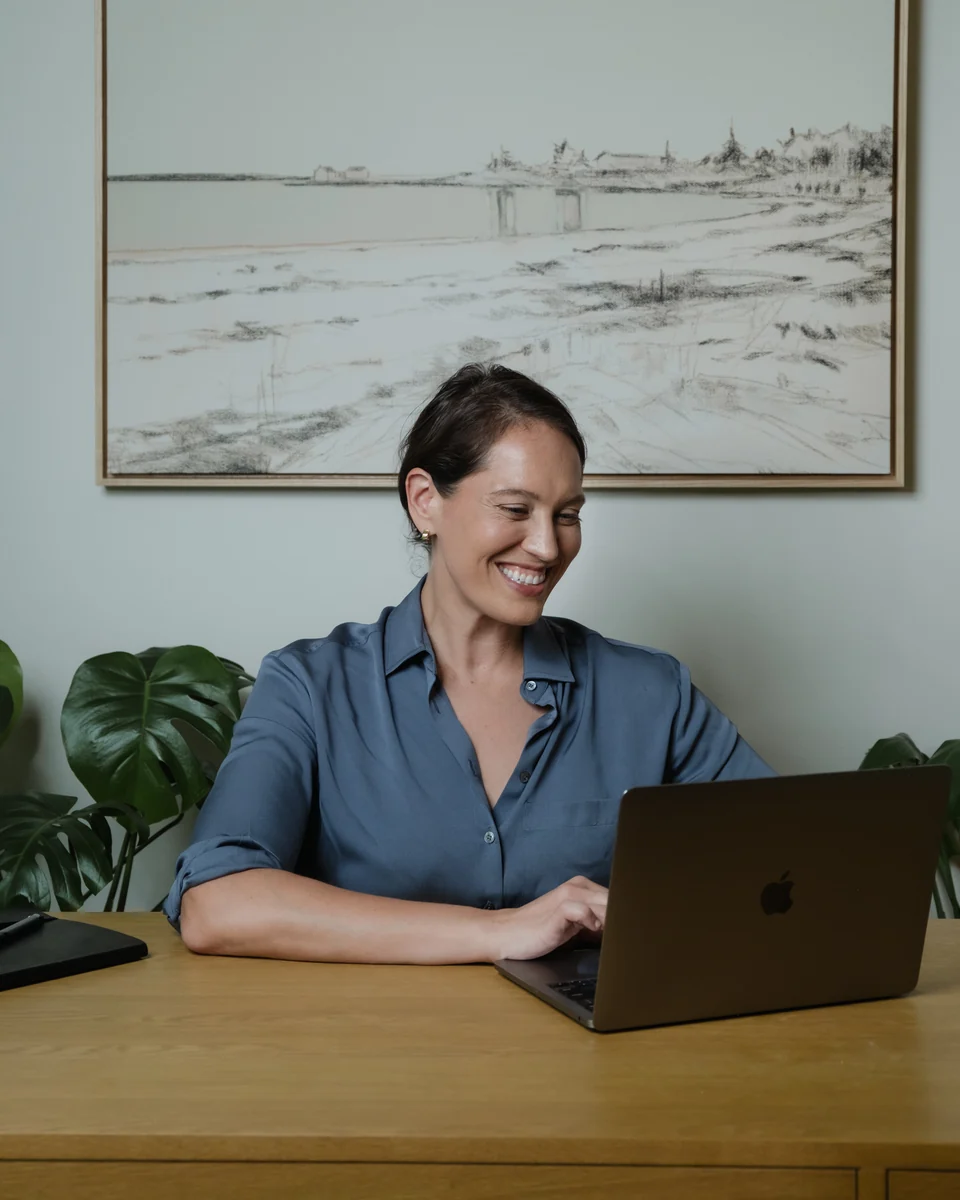 Annie Wright at her wooden desk, smiling as she works at her laptop.