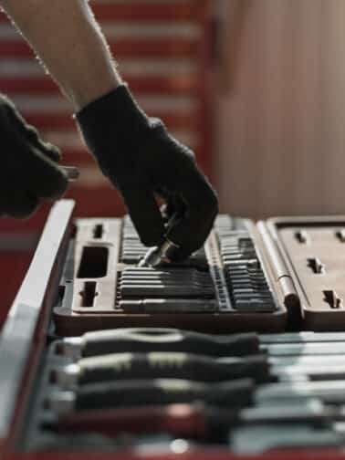 Mechanic in gloves taking tools and instruments out of a chest representing the biopsychosocial basics In a relational trauma self-care tool chest