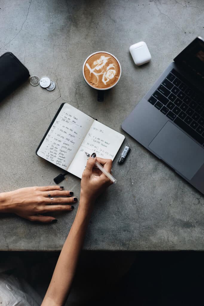 A person journaling beside a laptop and coffee, representing reflection and rebuilding self-awareness after trauma bonding.