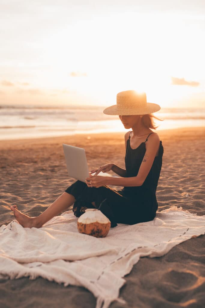 A woman sitting on the beach with a laptop at sunset, representing newfound peace and independence after healing from trauma bonding.