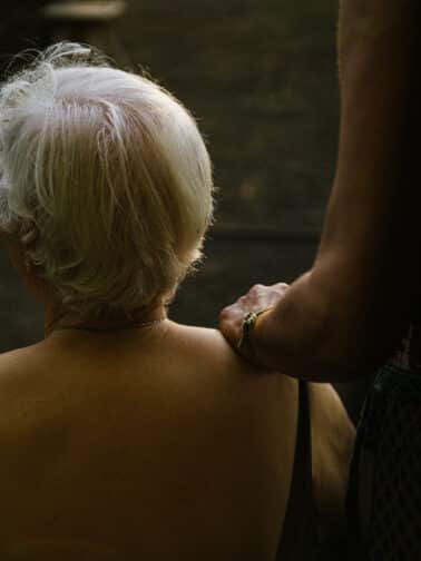 A younger person gently places a hand on an older woman’s shoulder, capturing the tenderness and complexity often present in relationships marked by intergenerational trauma.