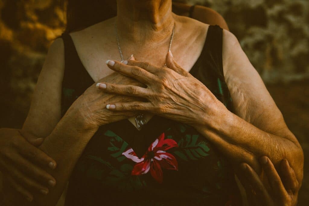 An older woman holding her hands to her chest while being gently embraced, symbolizing healing and connection after trauma bonding.