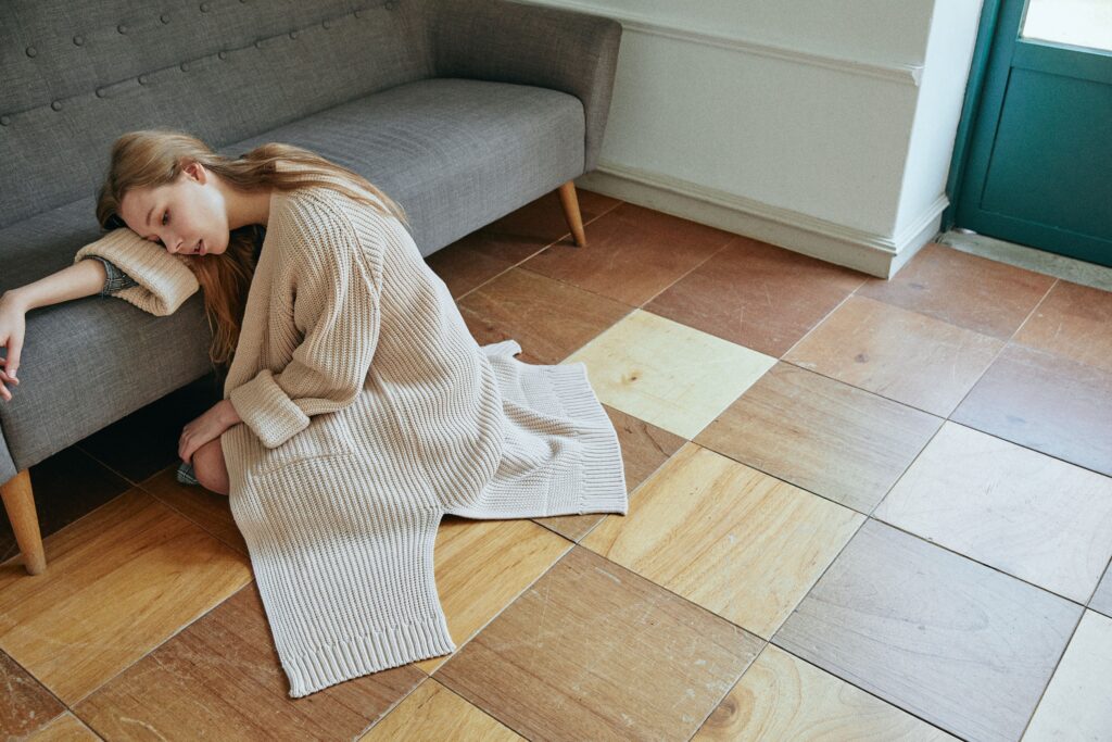 A woman sitting on the floor leaning against a couch, embodying the exhaustion and emotional collapse often felt after trauma bonding.
