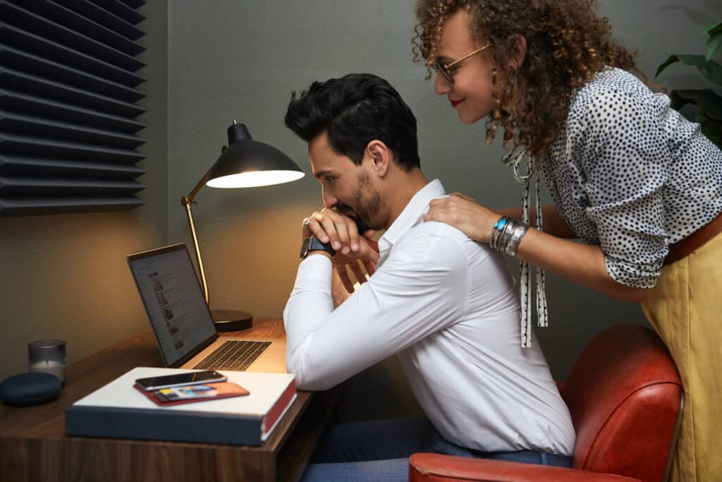 A woman leaning over a man at a desk, suggesting the subtle power imbalances and emotional control often present in trauma bonding.