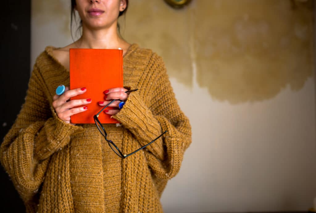 A person holds a closed journal and a pair of glasses, symbolizing reflection, grounding, and nervous system healing after trauma.