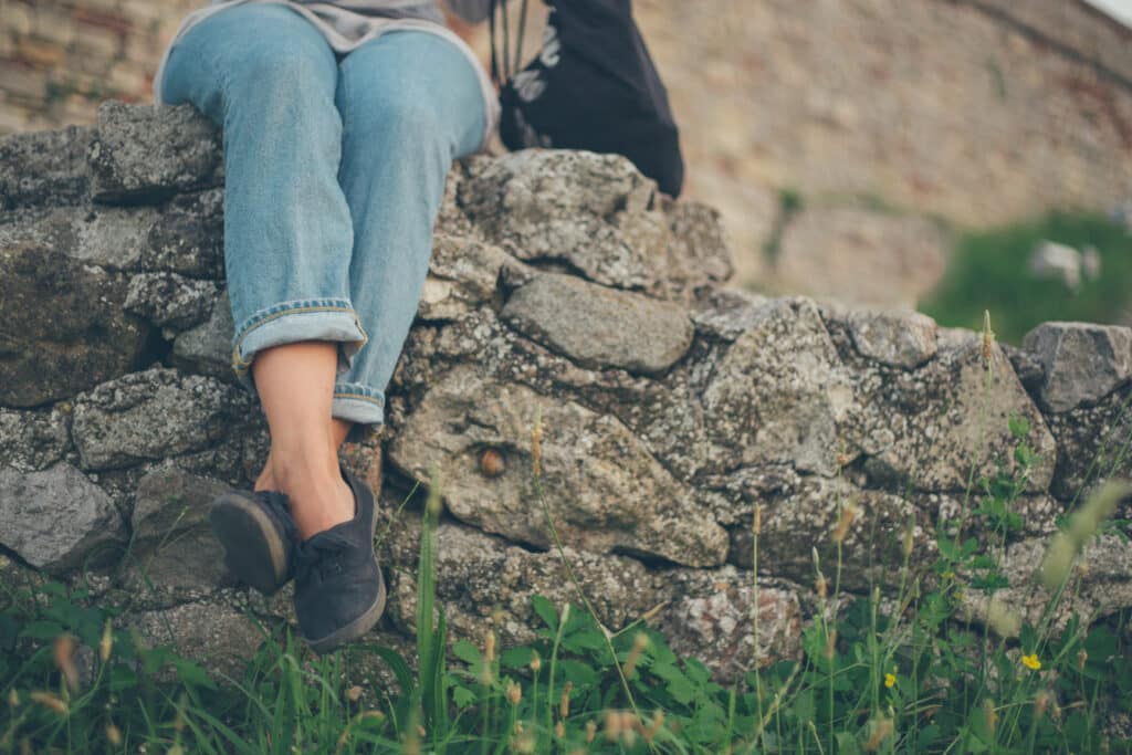 A person sits quietly on a stone wall with legs dangling, symbolizing stillness and the body’s effort to find safety after trauma.