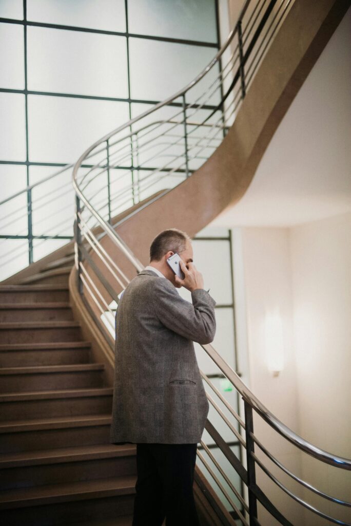 A man standing on a staircase talking on the phone, representing the tension and disconnection that can arise in trauma-bonded relationships.