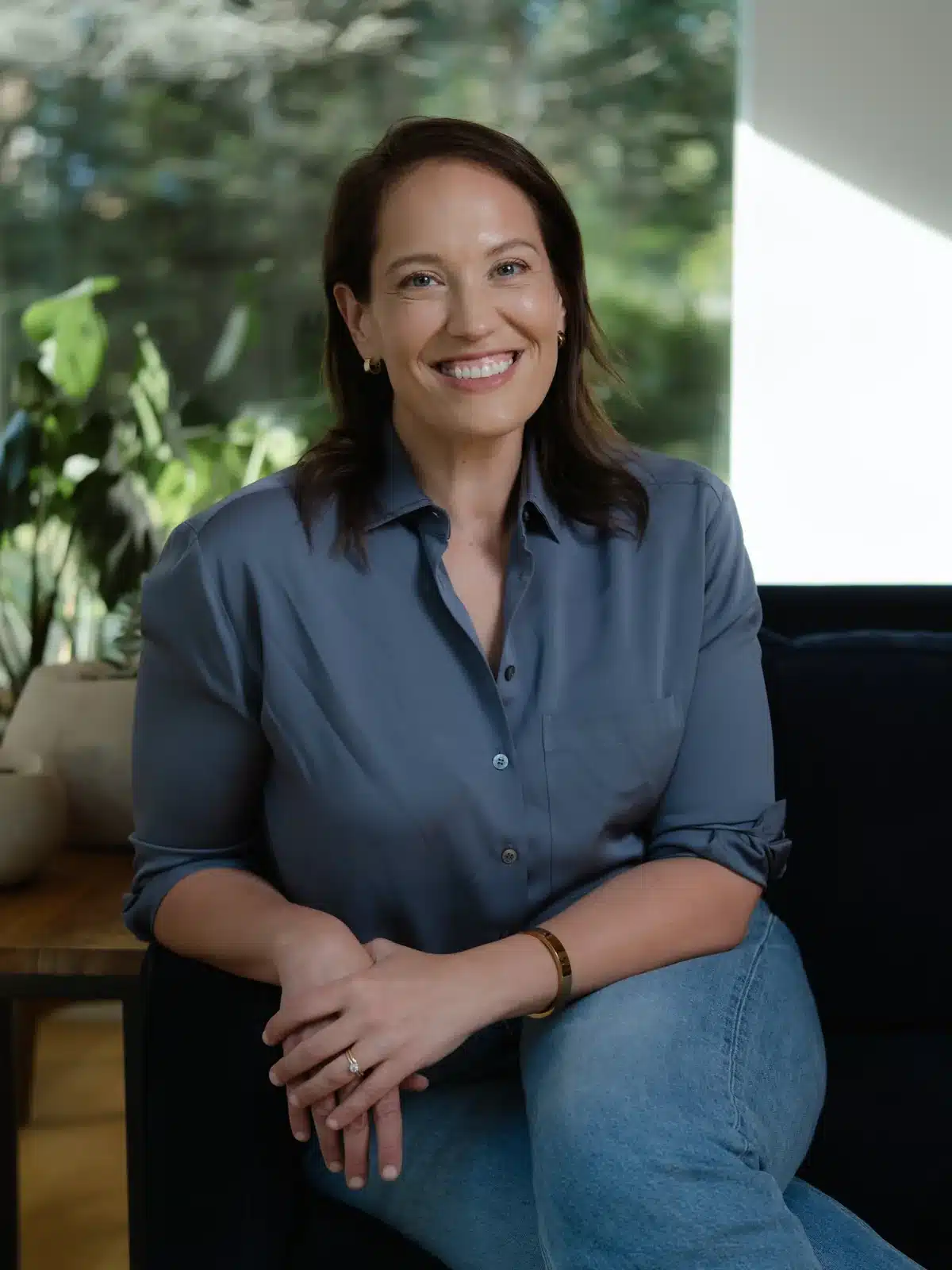 Annie Wright, LMFT, seated and smiling in a slate blue shirt beside a sunlit window
